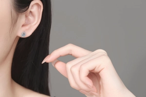 Close-up of elegant oval blue moissanite halo stud earrings worn on female ear model