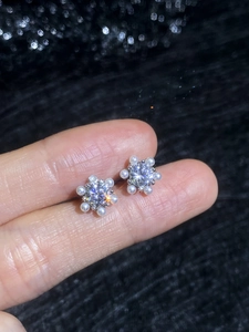 Macro detail of silver sunflower stud earrings with moissanite and pearls held by hand