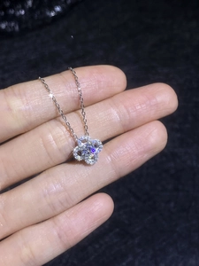 Vue rapprochée d'un pendentif en moissanite en forme de fleur tenu à la main sur fond noir