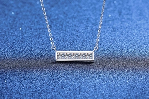 Vue macro d'un collier avec pendentif barre en argent et pierres sur fond bleu