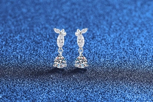 Macro shot of silver moissanite drop earrings with pear cut crystals on a blue surface