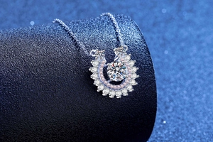 Macro shot of horseshoe silver pendant with round main stone and pink diamond halo