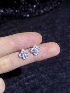 Detailed close-up of sparkling moissanite clover stud earrings held for size scale