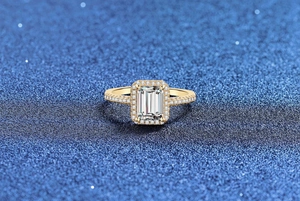 Makro-Detail des Smaragdschliff-Rings mit Halo-Fassung auf blauem Glitzerhintergrund