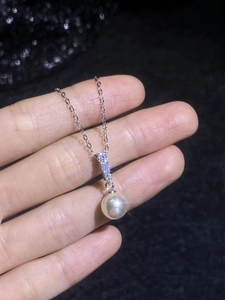 Détail d'une perle blanche ronde avec une bélière argentée sertie de diamants sur une chaîne