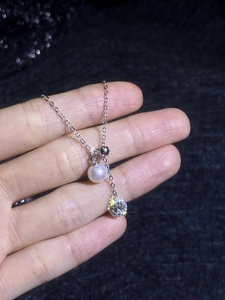 Detail shot of a S925 silver necklace featuring a white pearl and a round moissanite pendant