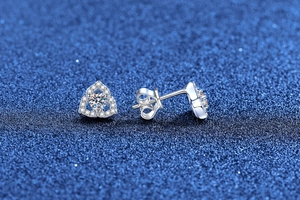 Detail view of heart-shaped S925 sterling silver moissanite studs on blue textured background