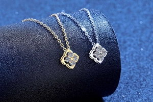 Detail of silver and gold four-leaf clover necklaces with pavé diamonds on a blue stand