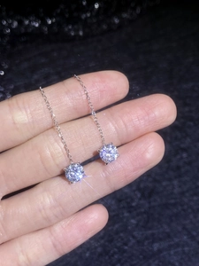 Detailed view of silver drop earrings with four-prong moissanite stones and fine chains