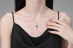 Detailed view of an elegant silver key pendant with floral pavé moissanite on a model