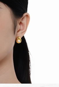 Macro side view of elegant gold oval stud earring with cream white pearl on ear
