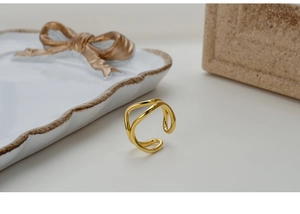 Detailed close-up of double-layered wavy gold ring on elegant ceramic background