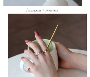Detail view of minimalist silver and gold curb link rings on a model holding a cup