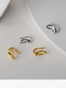 Detail of minimalist wavy gold and silver ear cuffs on a geometric prop background