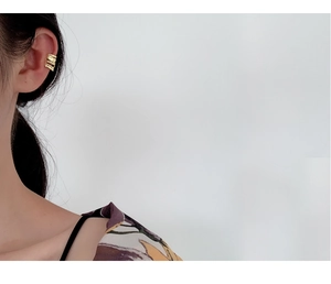 Vista dettagliata di un ear cuff dorato a strati indossato sulla cartilagine dell'orecchio