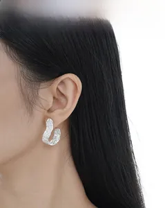 Detail of silver U-shaped earrings featuring a unique molten textured surface on a model