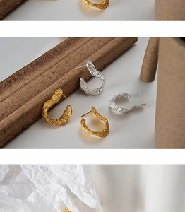 Detailed view of gold and silver stud earrings with molten lava texture on wooden prop