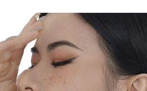 Close-up of realistic dark brown freckle tattoos and black eyeliner on female face
