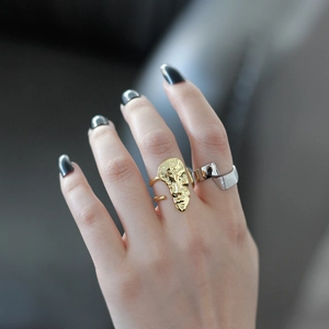 Artistic gold face mask ring and wide silver geometric open ring worn by a model