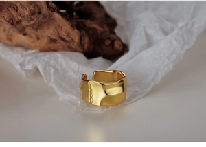 Detailed view of gold irregular wavy ring on white paper and rustic wood background
