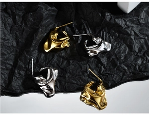 Detail of irregular liquid-style earrings in gold and silver finish with foil texture