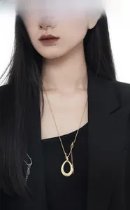 Vue détaillée du pendentif goutte doré texturé sur une longue chaîne avec un blazer noir