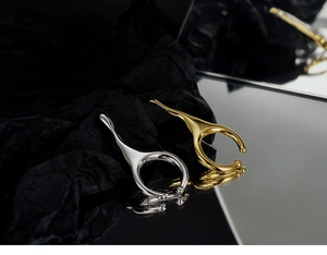 Polished silver and gold irregular C-shape ear cuffs shown on a mirror surface