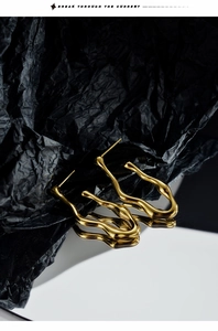 Detailed view of wavy gold-plated irregular earrings on a dark textured background