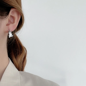 Minimalist irregular foil texture silver stud earring shown on a model's ear