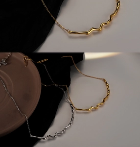 Detailed close-up of minimalist wave pendants in gold and silver on silk fabric