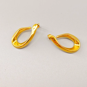 Détail de boucles d'oreilles géométriques dorées torsadées au fini métallique poli