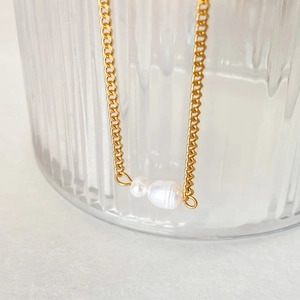 Gold stainless steel Cuban link necklace with baroque pearl pendant on textured glass background