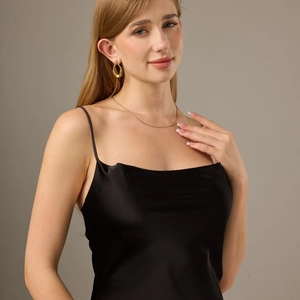Close-up of gold chunky teardrop earrings and a sleek black satin dress on a model