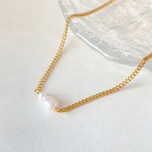 Detail of gold curb chain with double white pearl pendant on a minimal background