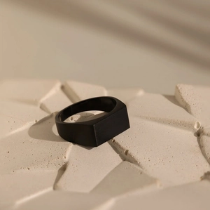 Detail of matte black square signet ring for men on a textured stone display