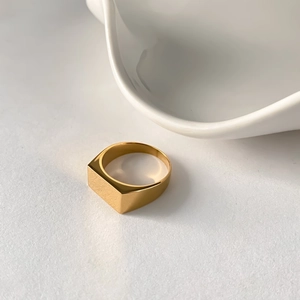 Close-up of a square signet ring with a polished gold finish on a minimalist background