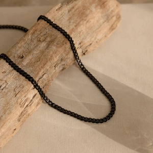 Primo piano della catena cubana nera opaca su legno strutturato con sfondo in tessuto beige