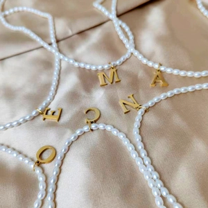 Nahaufnahme goldener Buchstabenanhänger an eleganten weißen Perlenkettensträngen