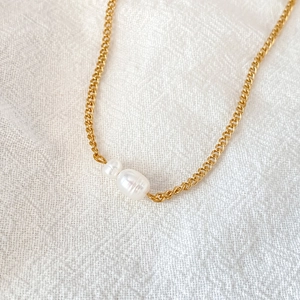Detail of gold Cuban chain necklace featuring two white baroque pearl pendants on linen