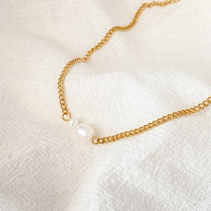 Detail of elegant gold chain necklace with round and baroque pearl pendants on white fabric