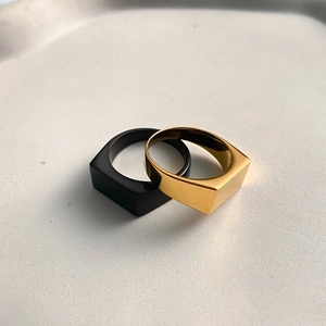 Macro shot of minimalist square rings in matte black and polished gold finishes