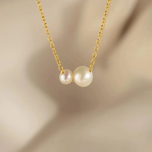 Collier en or élégant avec deux perles d'eau douce blanches sur un fond de tissu texturé