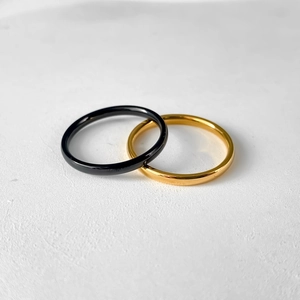 Close-up of 2mm black and gold stainless steel band rings on white background