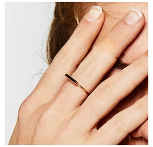 Detail view of a minimalist gold ring with a black rectangular inlay on a model's hand