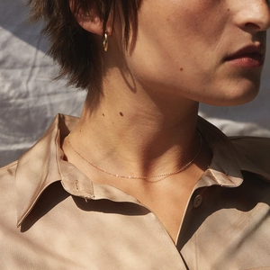 Détail d'un collier chaîne fine dorée minimaliste porté sur une chemise en soie