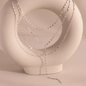 Three-layer silver layered necklace with Y-shaped tassel pendant on a white ceramic stand