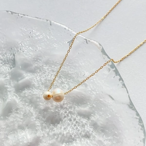 Détail macro du collier doré avec deux perles blanches sur surface en verre cristal