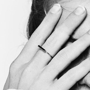 Artistic close-up of a minimalist silver ring with black bar inlay on female finger