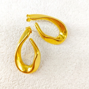 Détail de boucles d'oreilles géométriques torsadées dorées sur une texture blanche douce