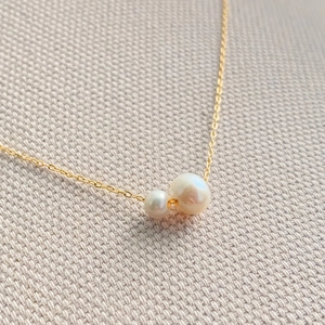 Vue macro d'un collier chaîne dorée minimaliste avec deux perles rondes blanches